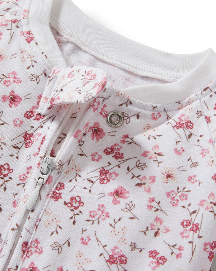 The Baby's Pima Peekaboo Romper in Dorset Floral features a white, long-sleeve, footless design with a pink floral pattern and white cuffs, displayed flat on a white background.