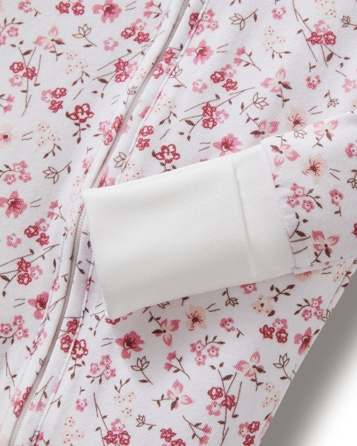 The Baby's Pima Peekaboo Romper in Dorset Floral features a white, long-sleeve, footless design with a pink floral pattern and white cuffs, displayed flat on a white background.