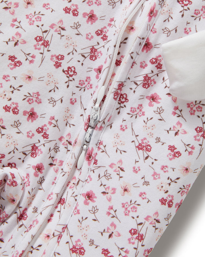 The Baby's Pima Peekaboo Romper in Dorset Floral features a white, long-sleeve, footless design with a pink floral pattern and white cuffs, displayed flat on a white background.