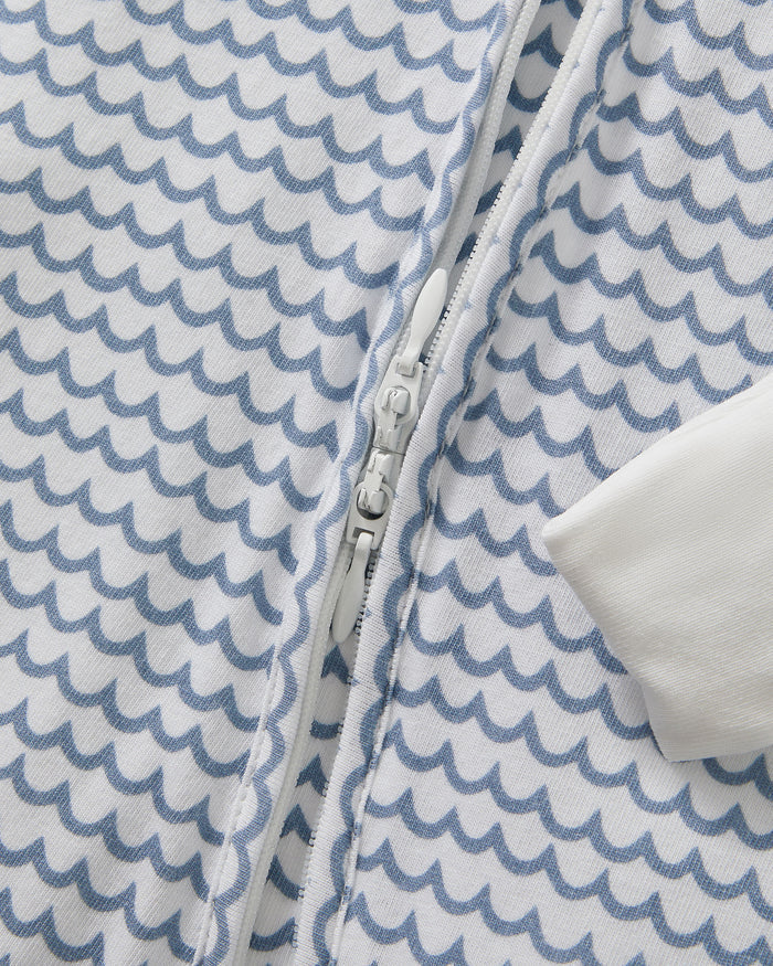 The Baby's Pima Peekaboo Romper in La Mer features a blue wave pattern, white cuffs on the sleeves and legs, and a diagonal zipper from the neckline to the left ankle.