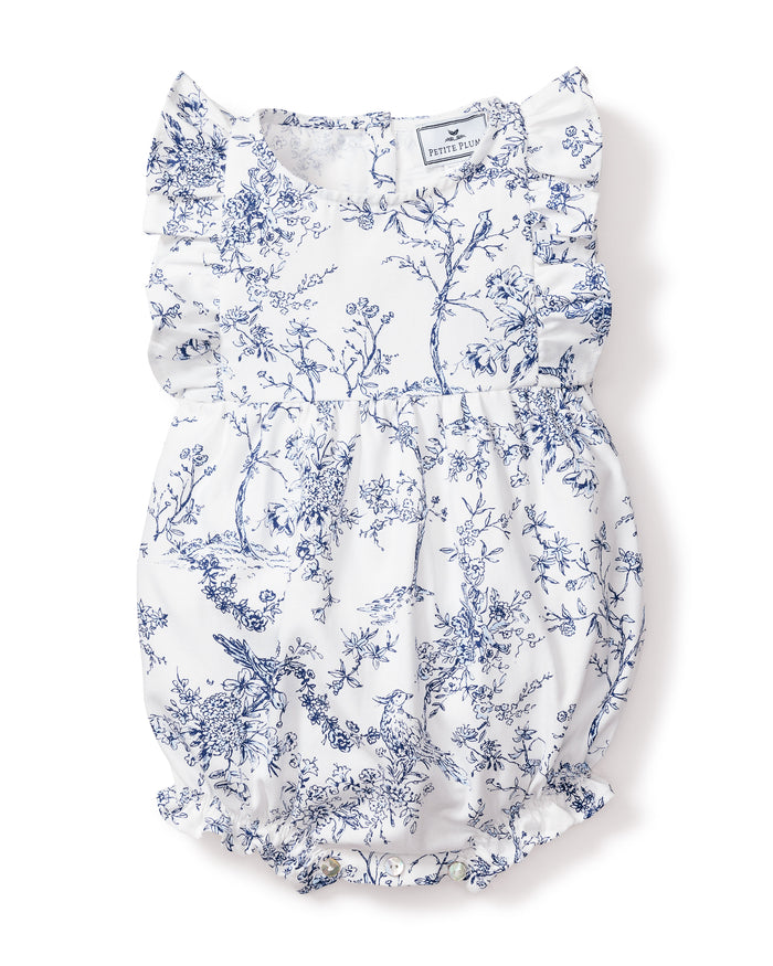 The Babys Twill Ruffled Romper in Timeless Toile by Petite Plume is a white romper with blue floral and botanical prints, ruffled sleeves, a cinched waist, and elastic leg openings for a gathered, airy look.