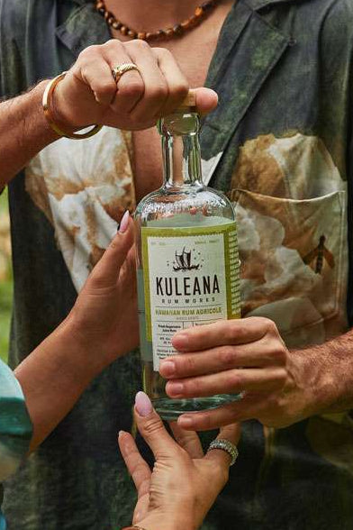 Man and woman holding a bottle of Kula Na`a rum outdoors