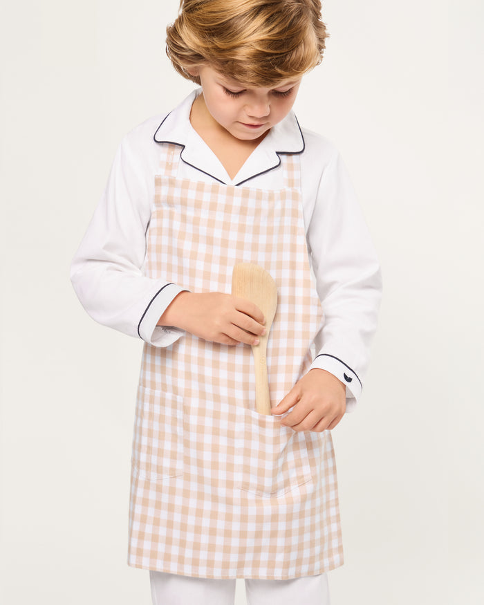 The Kid's Twill Apron in Camel Gingham, featuring a beige and white gingham pattern, two front pockets, and long waist ties, is displayed on a white background.