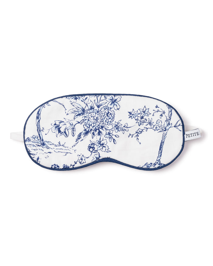 Enhance your sleep with Petite Plumes Kids Twill Sleep Mask in Timeless Toile, featuring a white background with blue floral toile patterns, delicate hand-drawn illustrations, elegant blue trim, and an elastic strap finished with a small label for added sophistication.