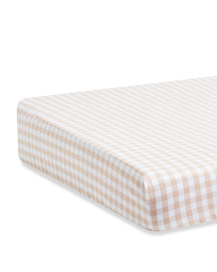 A close-up view of a mattress fitted with the Luxe Premium Percale Crib Sheet in Camel Gingham.