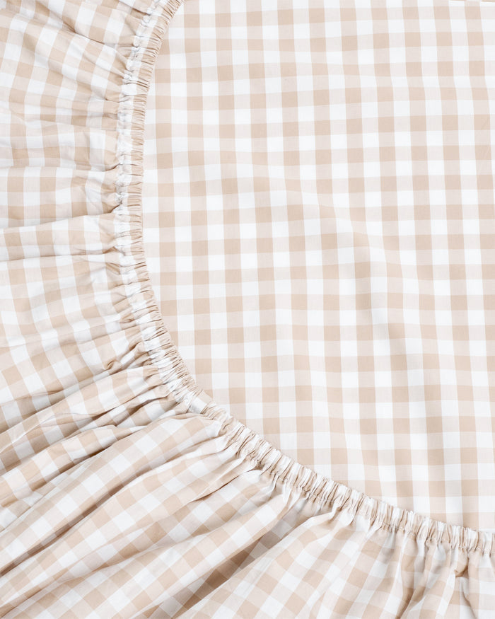 A close-up view of a mattress fitted with the Luxe Premium Percale Crib Sheet in Camel Gingham.