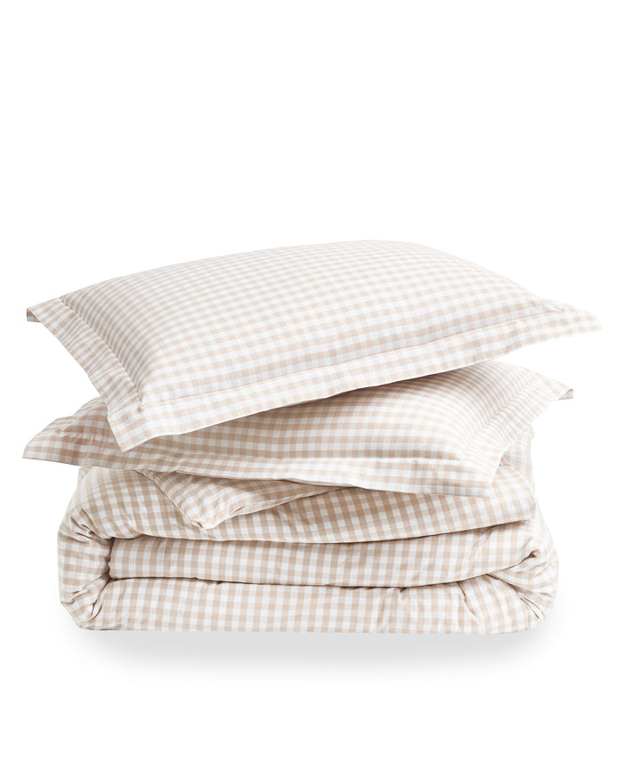 The Luxe Premium Percale Duvet Set in Camel Gingham features two pillows and a folded comforter with a beige and white gingham check pattern, neatly stacked on a white background.