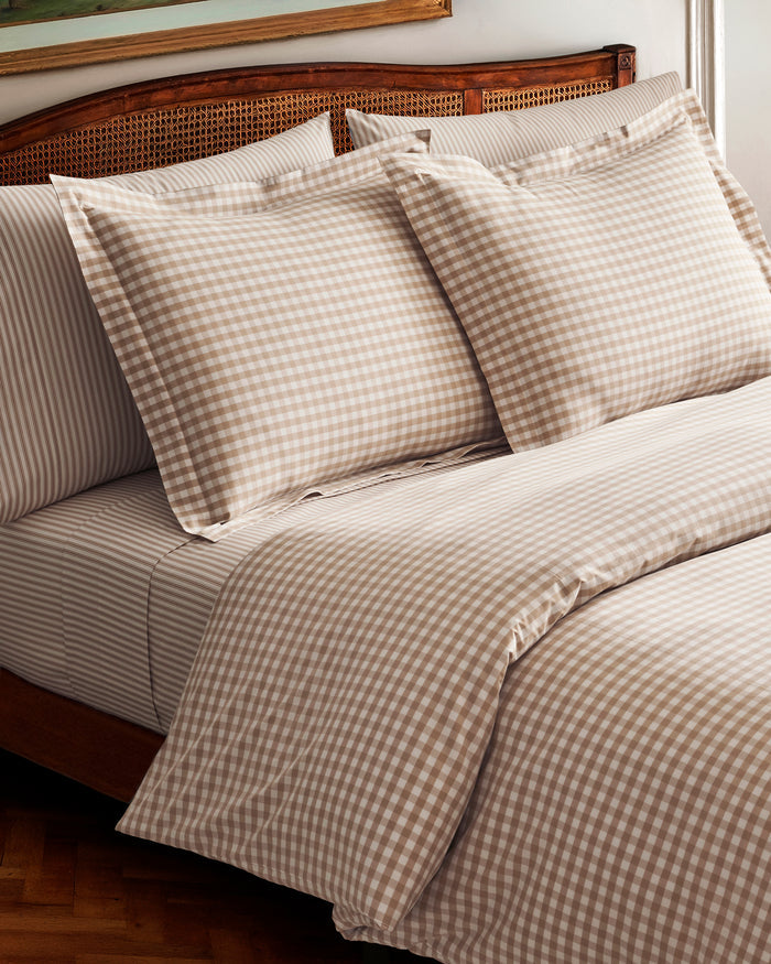 The Luxe Premium Percale Duvet Set in Camel Gingham features two pillows and a folded comforter with a beige and white gingham check pattern, neatly stacked on a white background.