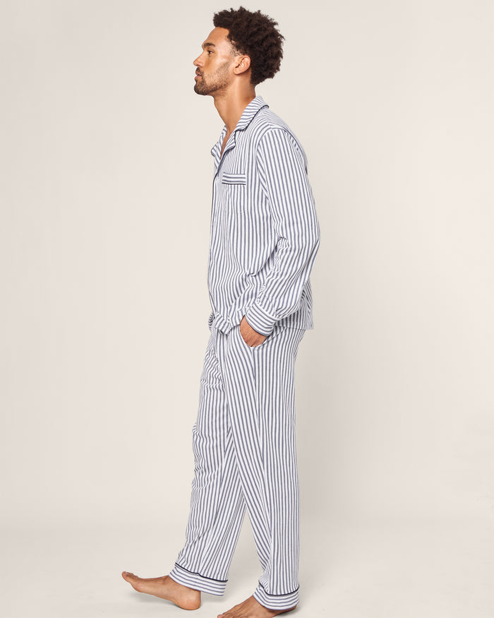 A man in profile wears the Petite Plume Mens Pima Pajama Set in Navy French Ticking, hands casually tucked in pockets, against a plain beige background.