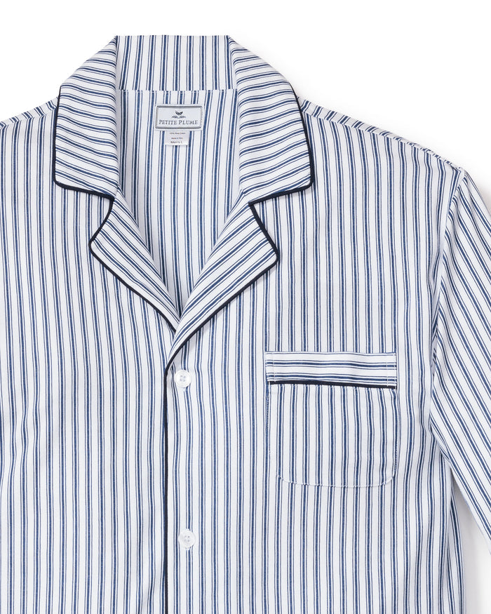A detailed view of the Mens Pima Pajama Set in Navy French Ticking from Petite Plume reveals blue and white striped luxuries. The top features a notched collar, chest pocket, button closure, dark blue piping, and an inner fabric label highlighting its classic design.