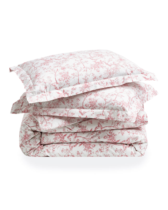 A neatly made bed features the Pink Timeless Toile Bedding Set with white sheets, a pink floral comforter, and two matching pillows against a curved, upholstered headboard in an elegant, classic bedroom.