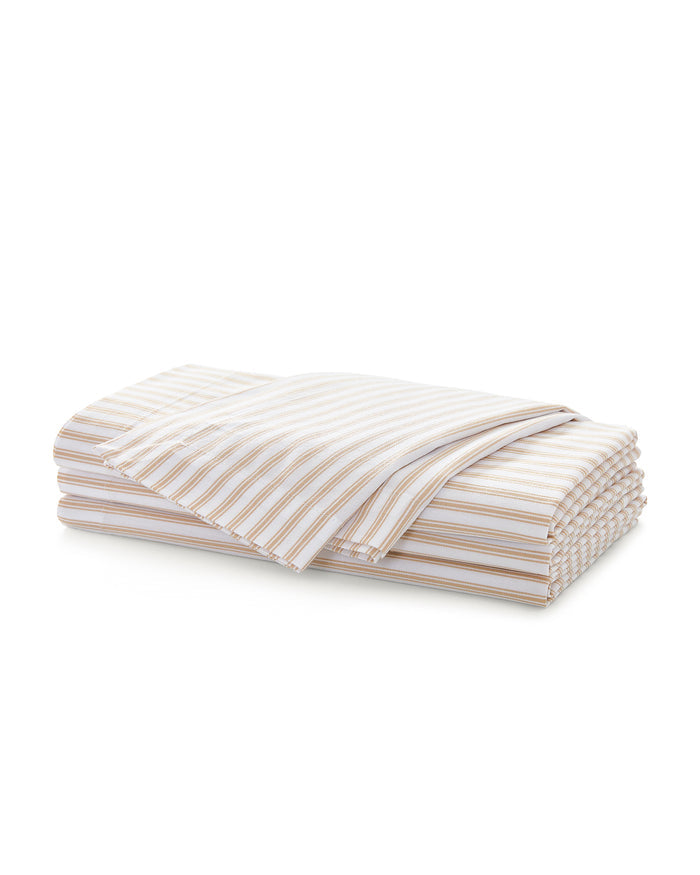 A neatly folded stack of Signature Twill Napkins in Camel Ticking, featuring thin beige and white stripes, displayed against a white background.