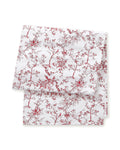 The Signature Twill Table Runner in Red Timeless Toile features a folded white fabric with a delicate red pattern of birds, trees, and branches.