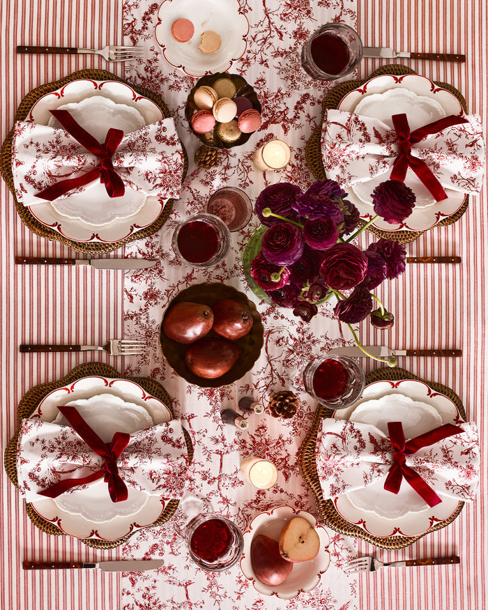 The Signature Twill Table Runner in Red Timeless Toile features a folded white fabric with a delicate red pattern of birds, trees, and branches.