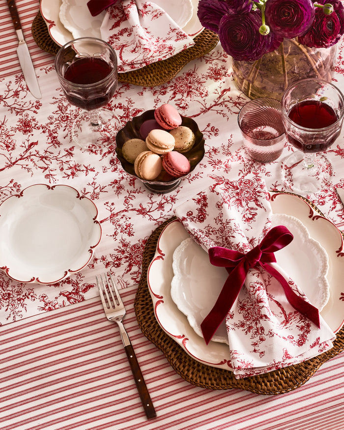 The Signature Twill Table Runner in Red Timeless Toile features a folded white fabric with a delicate red pattern of birds, trees, and branches.