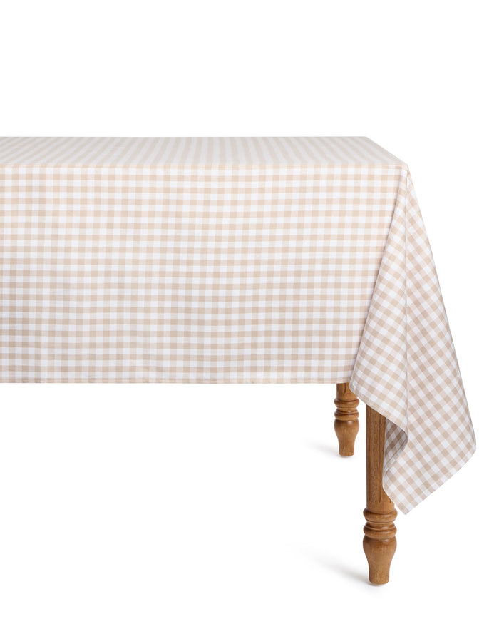 The Signature Twill Tablecloth in Camel Gingham, featuring beige and white checks, covers a rectangular table with wooden legs and drapes over the sides. The background is plain white.