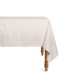The Signature Twill Tablecloth in Camel Gingham, featuring beige and white checks, covers a rectangular table with wooden legs and drapes over the sides. The background is plain white.
