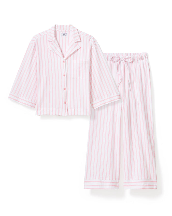 A person is seen in The Olivia Wide Leg Pima Pajama Set in Pink Stripe by Petite Plume, featuring a button-up top with a collar and long sleeves, and wide-leg pants made of luxurious Peruvian Pima cotton. The backdrop is plain and light-colored.