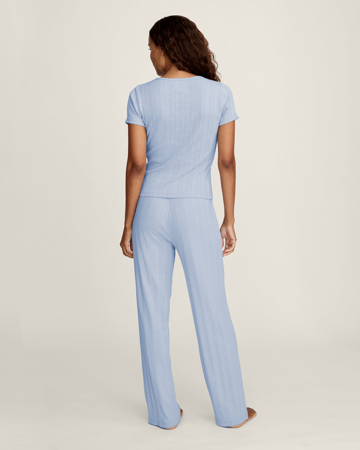 A woman with long wavy hair wears the Women's Pointelle T-Shirt in Periwinkle and matching pants, standing against a plain light background and looking at the camera with a slight smile.