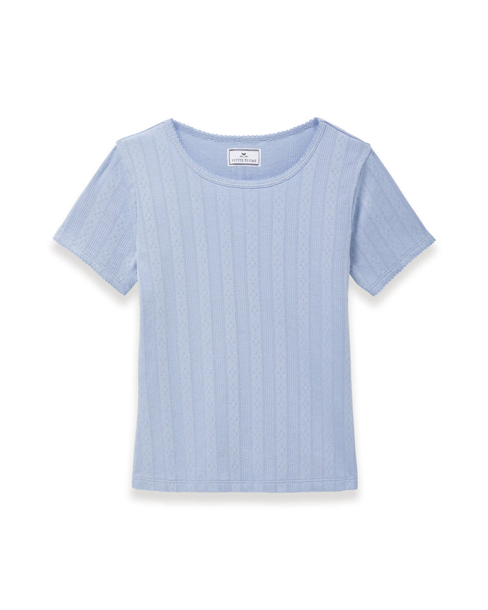 A woman with long wavy hair wears the Women's Pointelle T-Shirt in Periwinkle and matching pants, standing against a plain light background and looking at the camera with a slight smile.