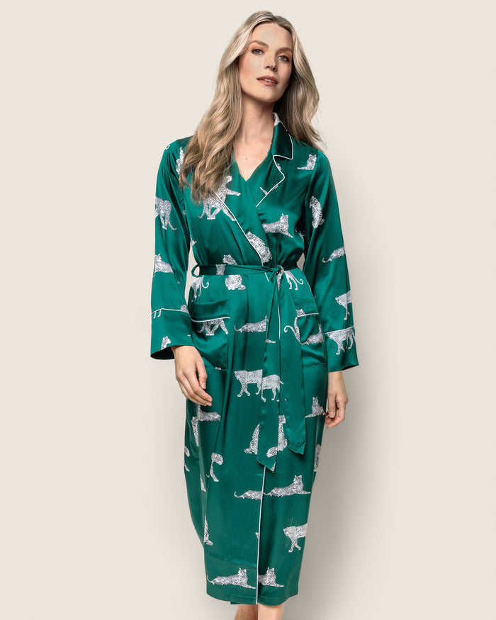 A person wears Petite Plumes Womens Silk Long Robe in Panthère de Luxe, a luxurious green robe featuring white leopard outlines. Adorned with piped edges, it includes a belt and long sleeves against a plain, light background.