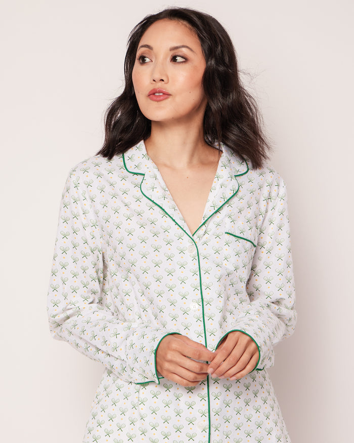 A person with long dark hair, wearing the Womens Twill Pajama Set in Match Point by Petite Plume, stands against a plain background. They gaze to the side thoughtfully, hands gently clasped.