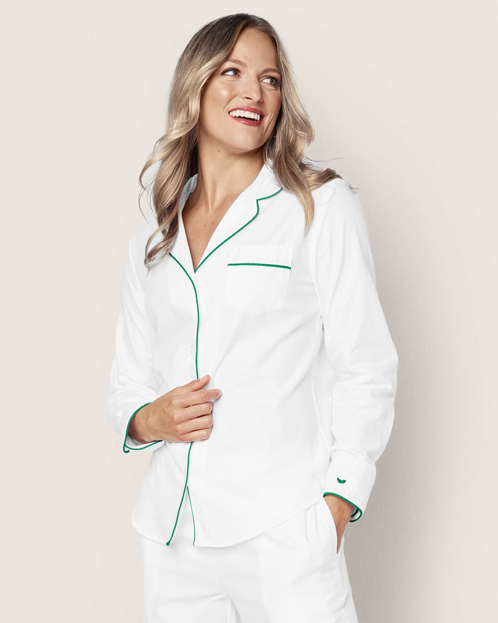 A smiling person with long blonde hair stands against a plain background wearing Petite Plumes Womens White Twill Pajama Set with Green Piping, casually slipping their hands into the 100% cotton pajama pants pockets.