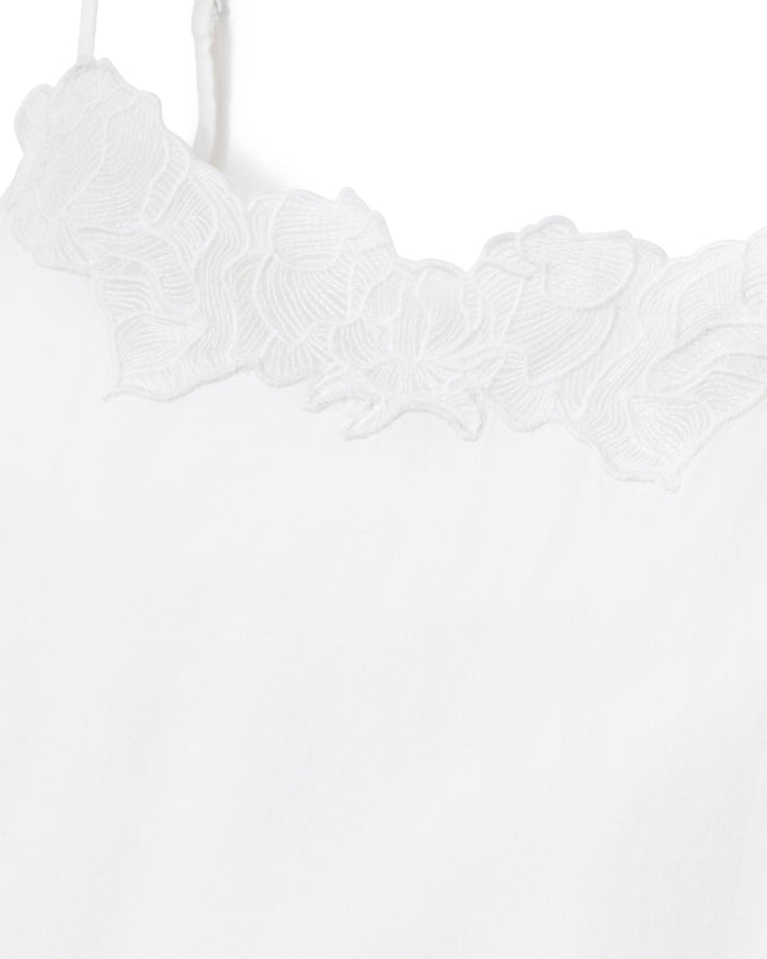 A woman with long, wavy hair stands barefoot against a plain light background, looking at the camera with a slight smile while wearing the Women's Voile Fleur Slip in White.